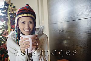 Asia Images Group - Woman in jacket and cap, holding mug in both hands