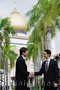 Asia Images Group - Two businessmen shaking hands, Mosque in the background