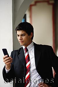 Asia Images Group - Businessman looking at mobile phone, leaning on wall