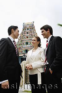 Asia Images Group - Two businessmen and one businesswoman standing, having a discussion, Hindu temple in the background