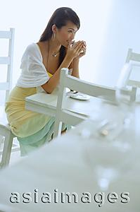 Asia Images Group - Woman sitting at cafe table, drinking from cup