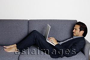 Asia Images Group - Businessman lying on sofa, using laptop