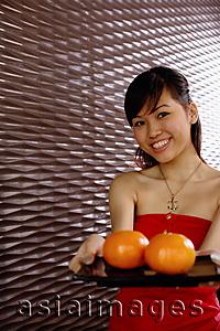 Asia Images Group - Young woman holding a tray with two oranges, smiling at camera