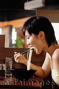 Asia Images Group - Young woman in restaurant, eating a bowl of noodles