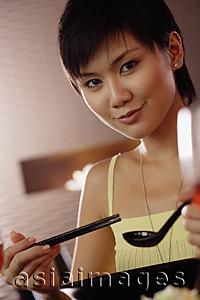 Asia Images Group - Young woman holding chopsticks and spoon, looking at camera