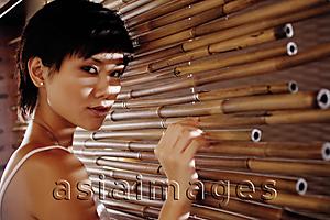 Asia Images Group - Young woman touching bamboo screen, looking at camera