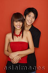 Asia Images Group - Couple standing against red wall, smiling at camera