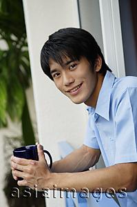 Asia Images Group - Young man leaning on railing, holding mug, smiling at camera