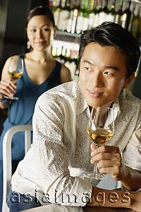 Asia Images Group - Man holding a drink, leaning on counter, looking away, woman in the background