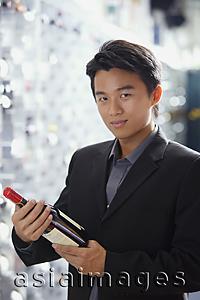 Asia Images Group - Man in wine cellar, holding bottle of wine, looking at camera
