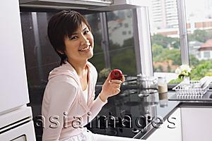 Asia Images Group - Young woman sitting on kitchen counter, holding an apple