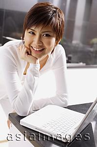 Asia Images Group - Young woman leaning on kitchen counter, hand on chin, laptop open in front of her