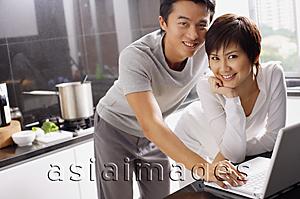Asia Images Group - Couple in kitchen, using laptop, smiling at camera