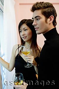 Asia Images Group - Couple holding wine glasses, looking away