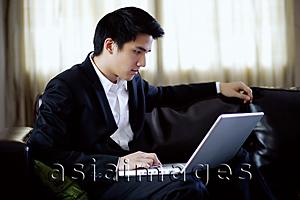 Asia Images Group - Man seating on sofa, using laptop, side view