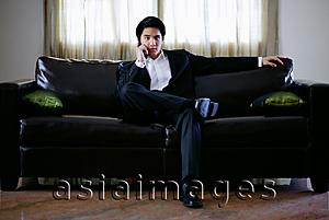 Asia Images Group - Man seating on sofa, using mobile phone