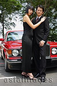 Asia Images Group - Well dressed couple standing in front of red car, woman with hands on man's shoulders