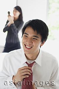 Asia Images Group - Man adjusting tie, smiling, woman in the background