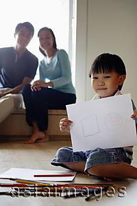 Asia Images Group - Young boy sitting on floor with drawing paper and coloured pencils, people in the background