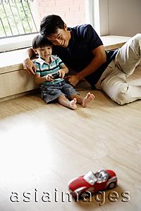 Asia Images Group - Father and young son sitting floor at home, playing with remote control car