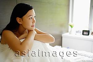 Asia Images Group - Woman sitting on bed, resting head on knees, looking away