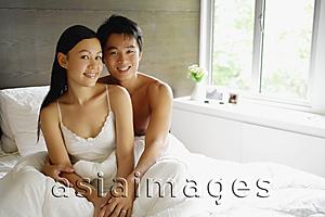 Asia Images Group - Couple sitting up in bed, looking at camera