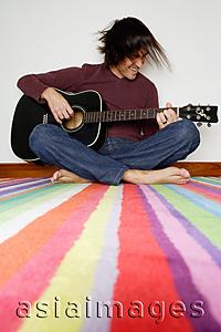 Asia Images Group - Man sitting on striped carpet, playing with guitar