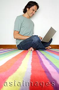 Asia Images Group - Man sitting on striped carpet, using laptop