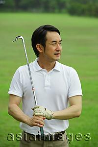 Asia Images Group - Man holding golf club, looking away