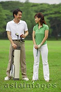 Asia Images Group - Man standing with golf bag, smiling at woman next to him