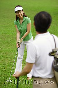Asia Images Group - Couple on golf course, woman preparing to swing, smiling at man in foreground