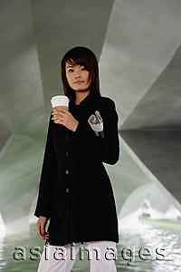 Asia Images Group - Woman in black jacket, holding disposable coffee cup and newspaper