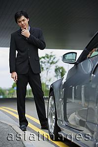 Asia Images Group - Businessman with hand on chin, looking at car