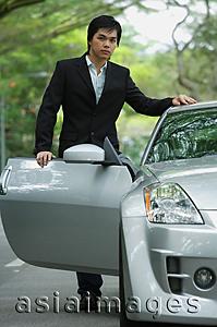 Asia Images Group - Businessman opening car door, looking at camera