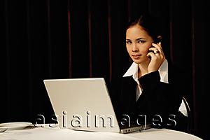 Asia Images Group - Businesswoman sitting in restaurant using mobile phone and laptop, looking at camera