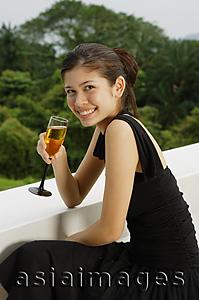 Asia Images Group - Young woman leaning on ledge, holding champagne glass