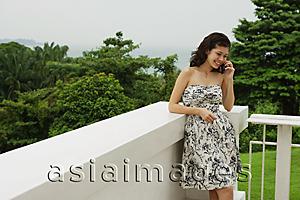 Asia Images Group - Young woman in floral dress, standing on balcony, using mobile phone