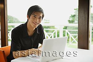 Asia Images Group - Man in cafe using laptop, smiling at camera