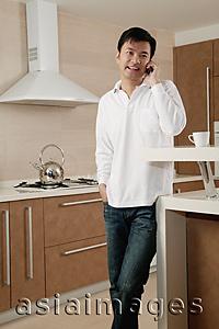Asia Images Group - Man standing in kitchen, using mobile phone