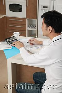 Asia Images Group - Man sitting at kitchen counter with calculator and bills