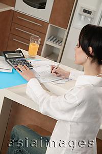 Asia Images Group - Woman sitting at kitchen counter with calculator and bills