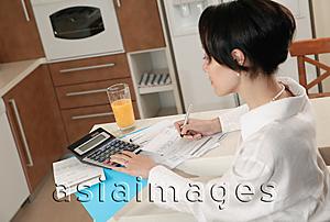 Asia Images Group - Woman sitting at kitchen counter doing finances
