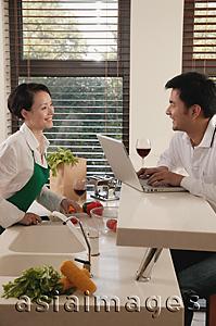 Asia Images Group - Couple in kitchen, woman chopping vegetables, man using laptop
