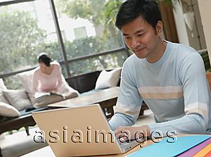 Asia Images Group - Man using laptop, woman in background reading