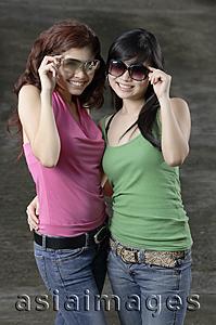 Asia Images Group - Two teenage girls, standing side by side, adjusting sunglasses