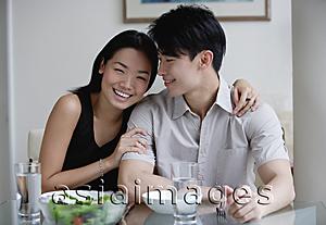 Asia Images Group - Couple at home, sitting by dining table, woman looking at camera