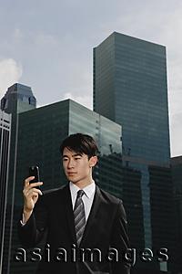 Asia Images Group - Businessman looking at mobile phone, cityscape in the background