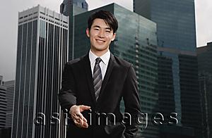 Asia Images Group - Businessman holding hand out toward camera, buildings in the background