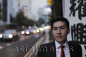 Asia Images Group - Young man standing by busy road in the evening.