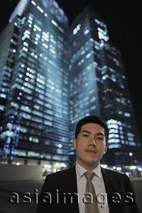 Asia Images Group - Man wearing a suit standing in front of lit buildings at night